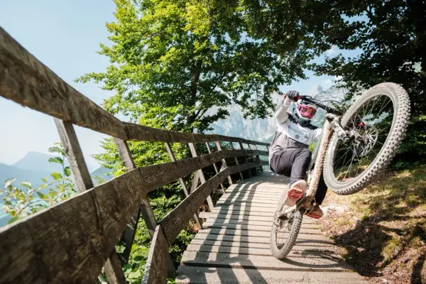 Ciclista in azione durante il giro del lago di Molveno in bici, su un ponte di legno tra alberi verdi e montagne.